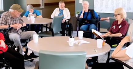 A small group of seniors gathers around round tables in a bright common room at Arbor Terrace Lakeway, engaged in a structured activity with a staff member — memory care Lakeway TX.