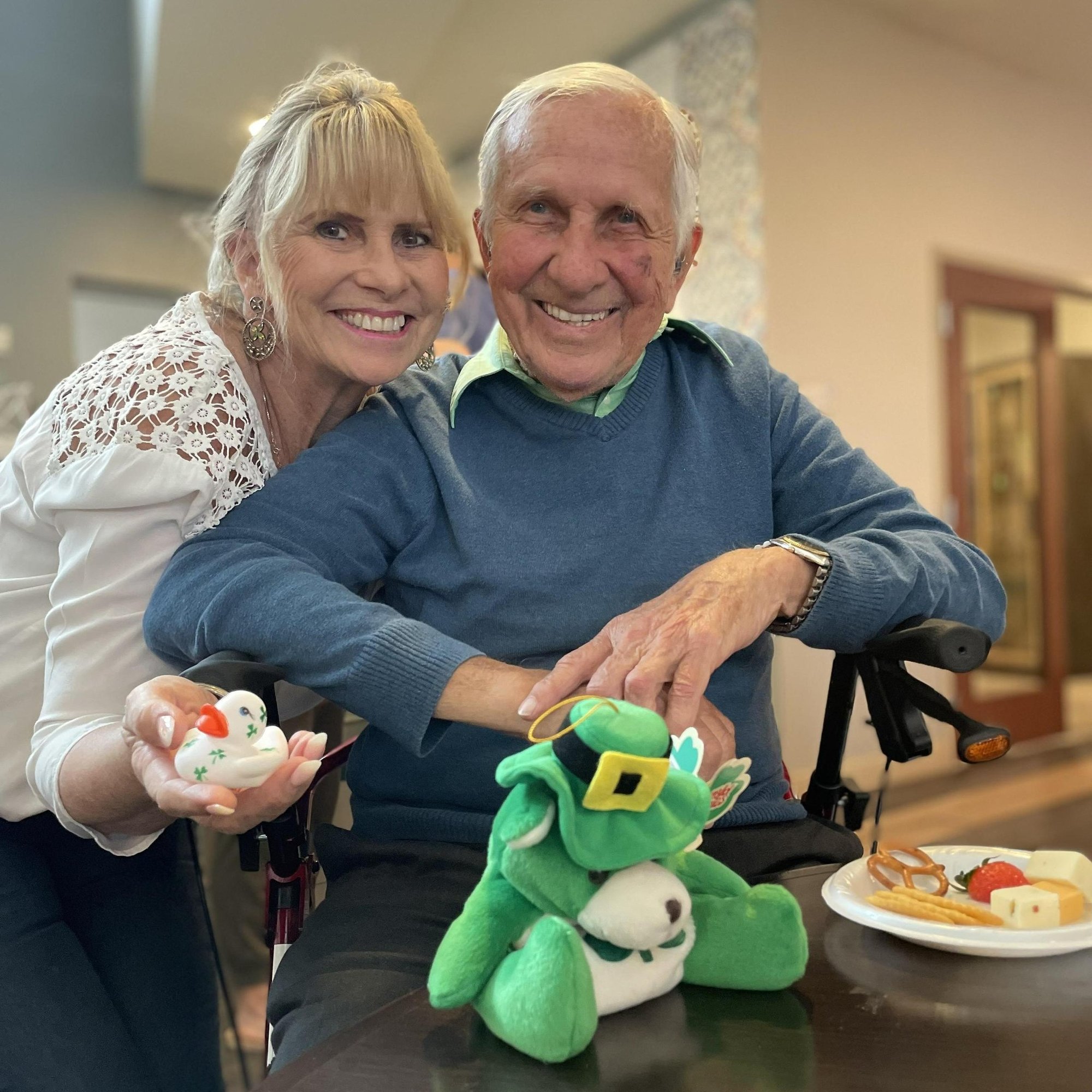 Two residents smile warmly while holding a festive stuffed animal during a St. Patrick's Day celebration at Arbor Terrace Lakeway TX, reflecting the joyful, holiday-filled community life at this assisted living community.