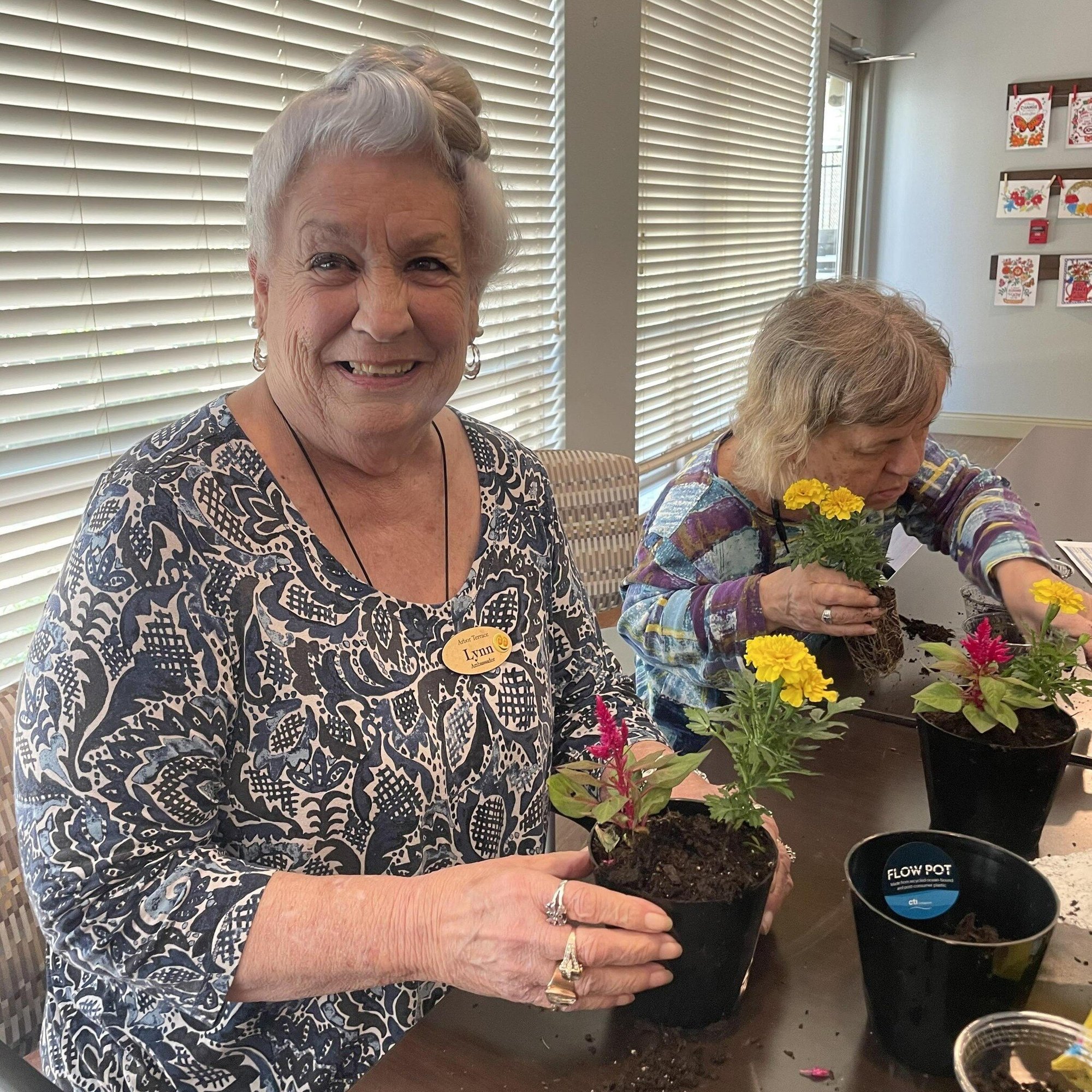 A staff member and a resident work together potting colorful flowers at this senior living community in Lakeway, TX, enjoying a hands-on gardening activity that nurtures creativity and connection at Arbor Terrace.