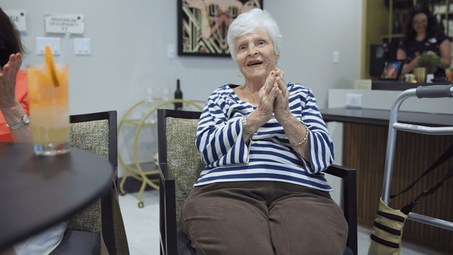 Resident sitting in a chair smiling and clapping her hands 
