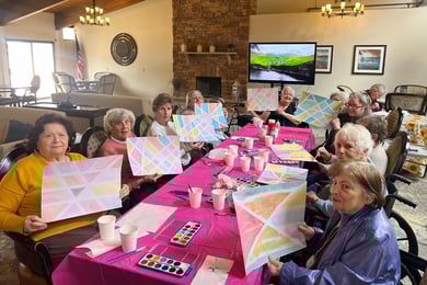 residents of Arbor Terrace Middletown smile and sit at a pink table as they show off their colorful watercolor paintings