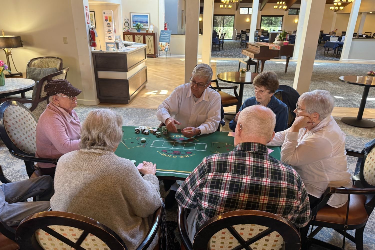 a group of residents from Arbor Terrace Middletown sit around a poker table and play cards