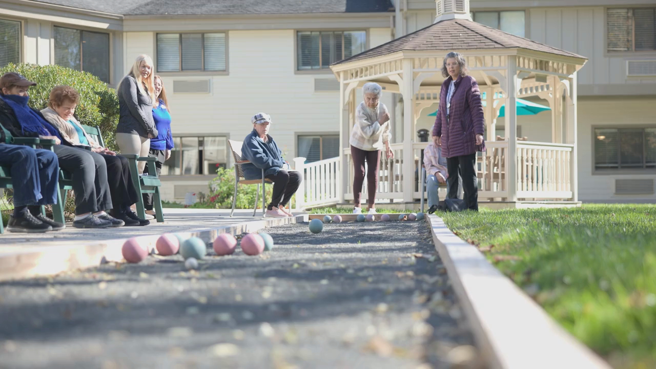 Residents and family members enjoy a friendly game of bocce ball on a sunny day at this assisted living Middletown NJ community, with a charming gazebo and well-kept grounds in the background.