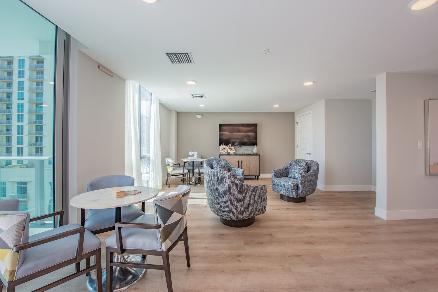 A sunlit lounge area at Mirabelle senior living in Miami, FL, featuring floor-to-ceiling windows, comfortable seating, and an open, airy layout ideal for active senior living.