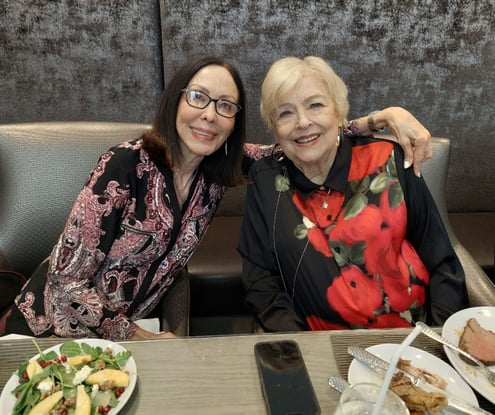 Two women smiling warmly over a shared meal at a senior living community in Miami, FL, enjoying fresh, beautifully presented dishes together in a welcoming dining setting.