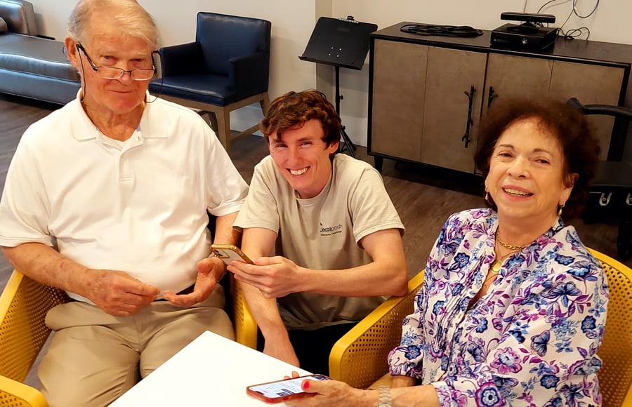Two older adults and a younger visitor share a warm, cheerful moment together in a comfortable common area at Mirabelle, a welcoming assisted living community in Miami, FL where family connections are cherished.