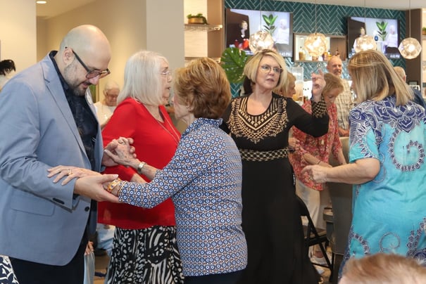 A group of residents dance together in a beautifully decorated common area, capturing the lively social calendar and warm community spirit at this senior living community in Miami, FL.