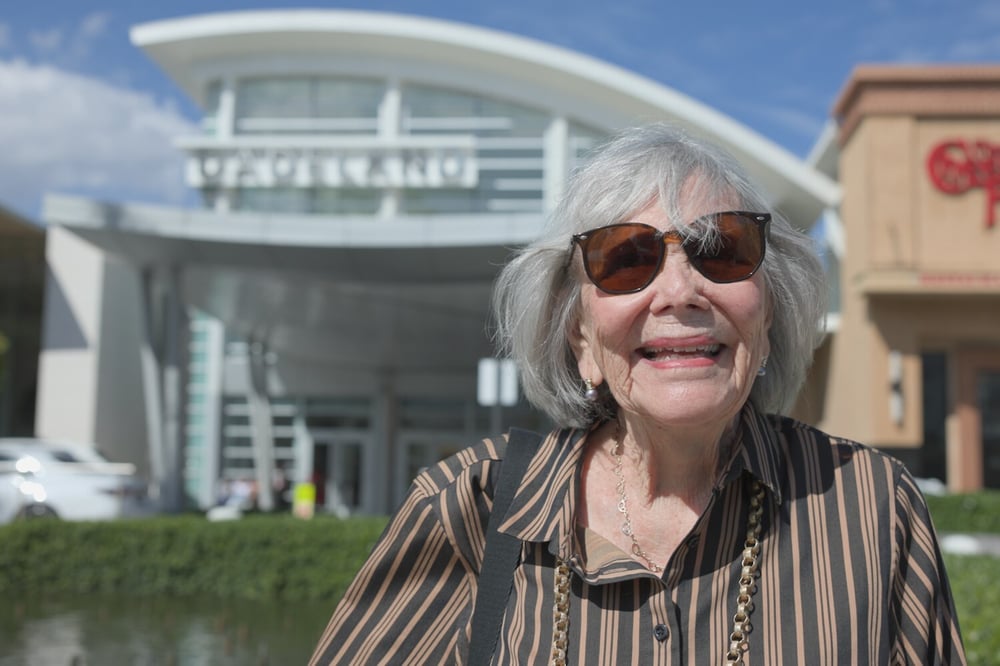 A senior woman smiles warmly while standing outside a building during an outing, reflecting the active senior lifestyle at The Arbor Company.
