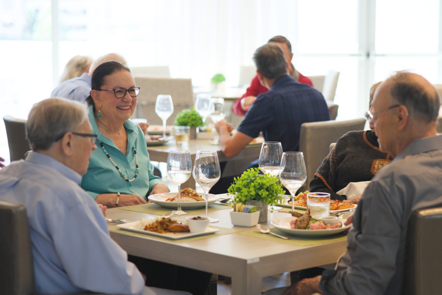 Residents enjoy a lively conversation over a chef-inspired meal at a beautifully set table, capturing the community connection and active senior lifestyle at The Arbor Company.