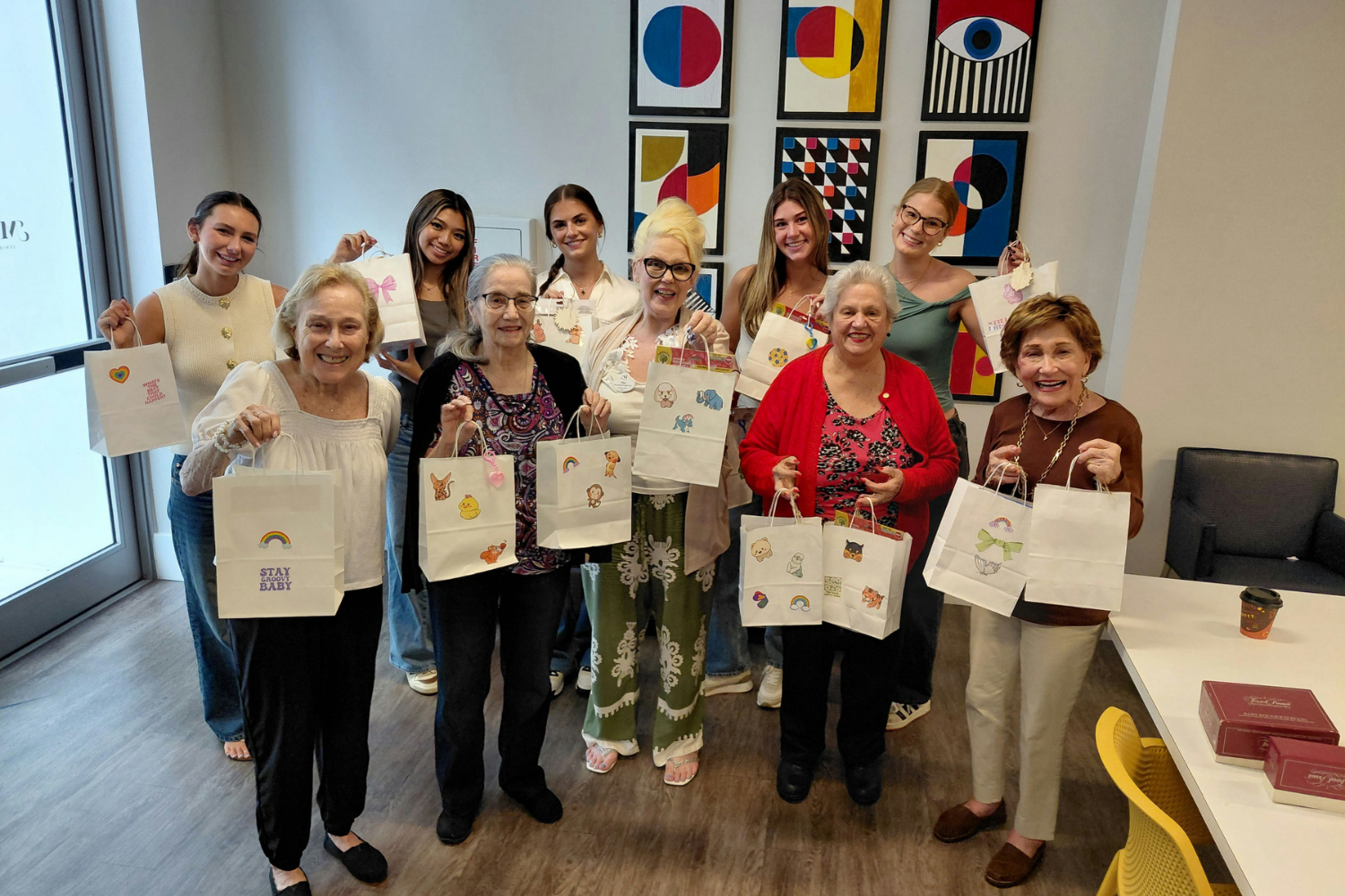 A group of seniors and staff members proudly display handmade tote bags after an arts and crafts class at Mirabelle, an active senior living community in Miami, FL.