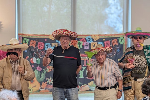 Residents laugh and pose in festive sombreros and props at a themed party at Mirabelle, a vibrant senior living community in South Miami, FL where fun social activities and lively celebrations are part of everyday life.