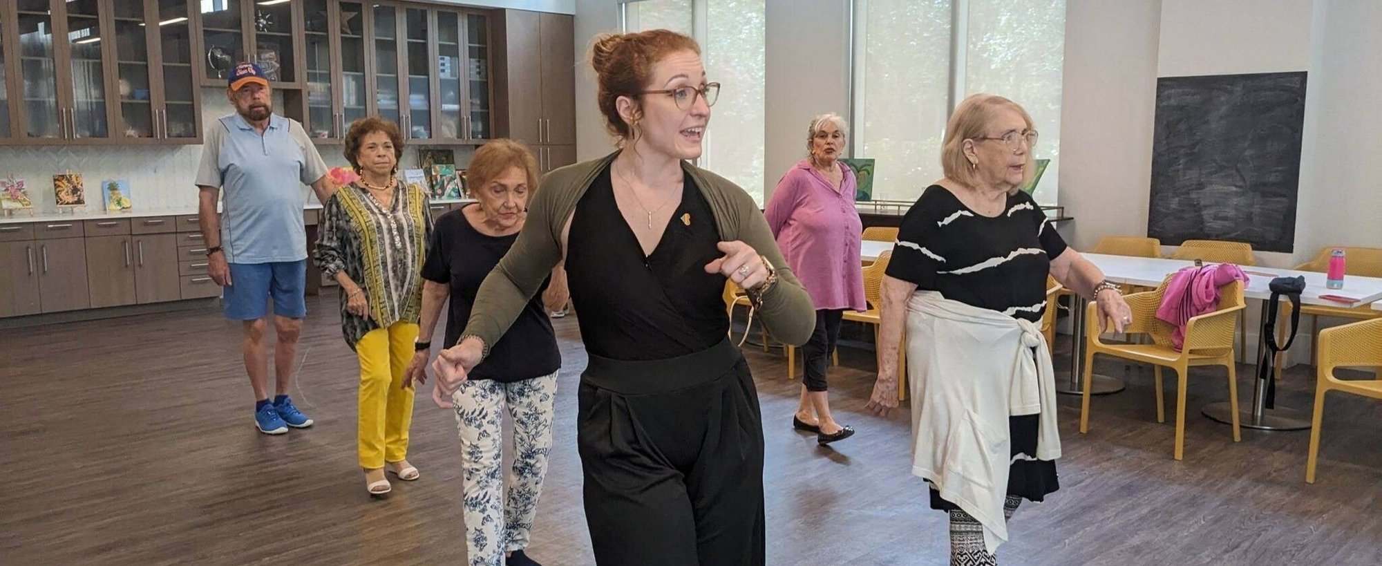 Seniors and a staff member enjoy an energetic movement class together in a bright, open activity room at Mirabelle, a senior living community near Coral Gables, FL, offering engaging wellness programs for active older adults.