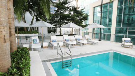 A sparkling outdoor pool surrounded by lounge chairs, umbrellas, and lush palm trees at Mirabelle, a resort-style senior living community in Miami, FL where residents enjoy a relaxed, sun-filled lifestyle.