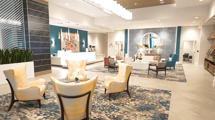 A welcoming lobby lounge at Mirabelle senior living in Miami, FL, with curved upholstered seating, warm lighting, and an open layout creating a warm atmosphere for residents and visitors.