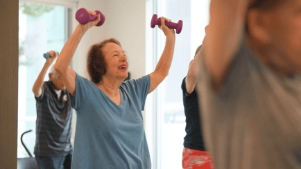 Resident in a fitness class lifting hand weights above her head 