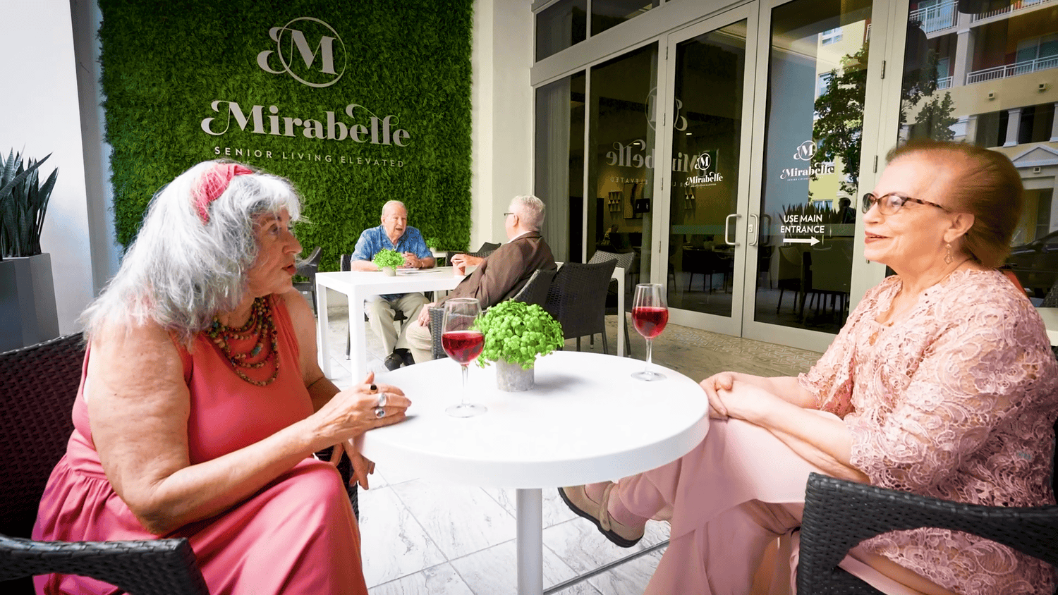 Residents enjoy drinks and conversation at an outdoor patio table at Mirabelle senior living in Miami, FL, embracing the vibrant social lifestyle of senior living near South Miami.