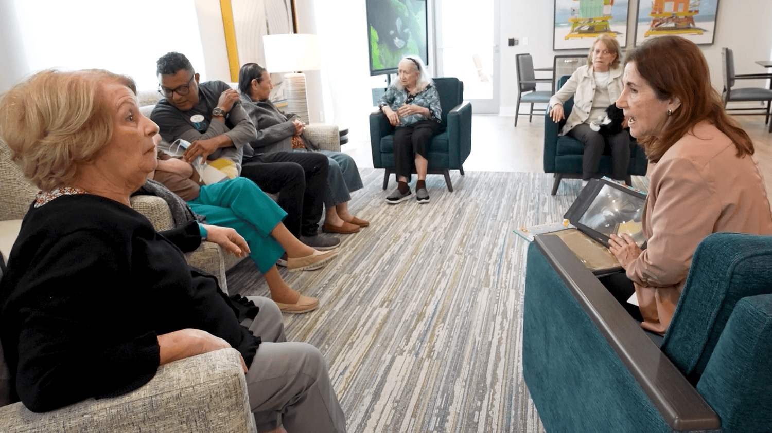 Residents and staff gathered in a bright, comfortable common area, sharing a warm conversation — reflecting the welcoming community atmosphere at a senior living community in Miami, FL.