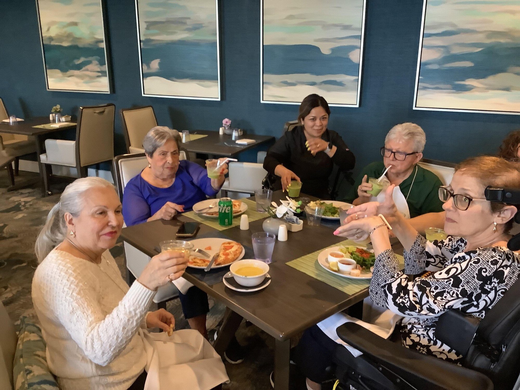 Residentes comparten bebidas y una comida en el comedor de Mirabelle, disfrutando del ambiente social y cálido de nuestra comunidad de vida independiente en Miami, FL.