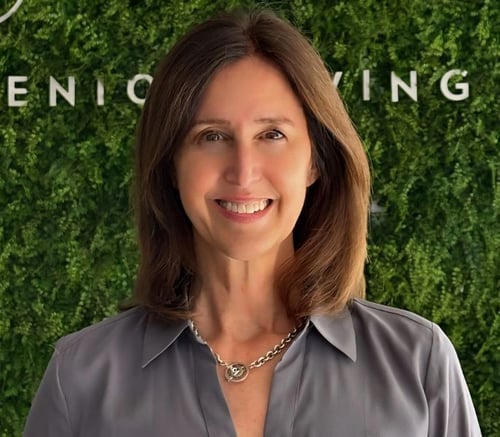 A smiling staff member at Mirabelle senior living in Miami, FL, posing in front of a lush green living wall with "Senior Living" signage in the background.