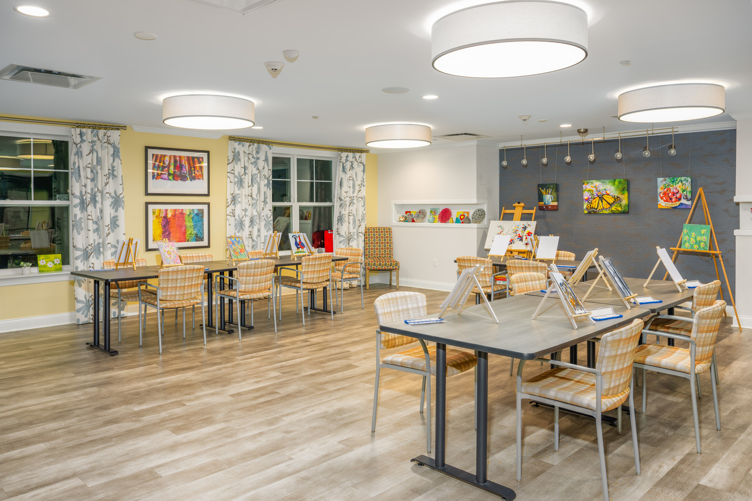 a space for arts and crafts with tables and chairs in Arbor Terrace Monmouth. the room has art hanging on the walls