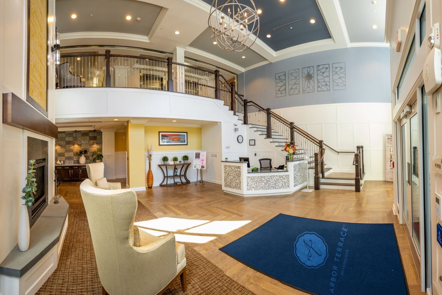 The bright, open lobby and front desk area of this senior care Shrewsbury New Jersey community, with a curved staircase, high ceilings, warm flooring, and a welcoming reception area at the heart of the community.