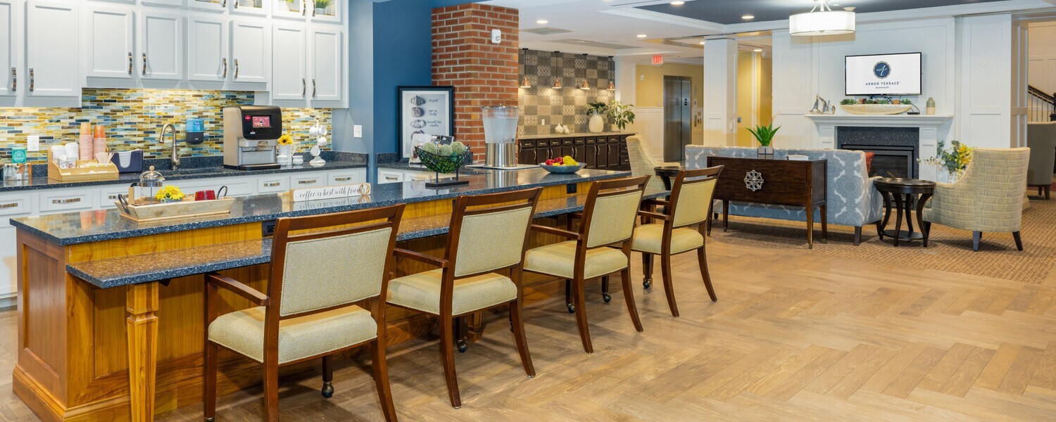 An open kitchen and gathering space at this senior living Shrewsbury NJ community featuring warm wood tones, a stone fireplace, open shelving, and island seating — ideal for connection and an active senior lifestyle Shrewsbury NJ.