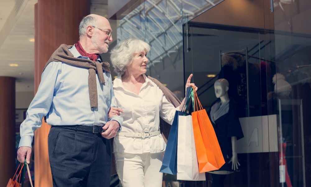 senior man and woman holding shopping bags. woman pointing at store to their side