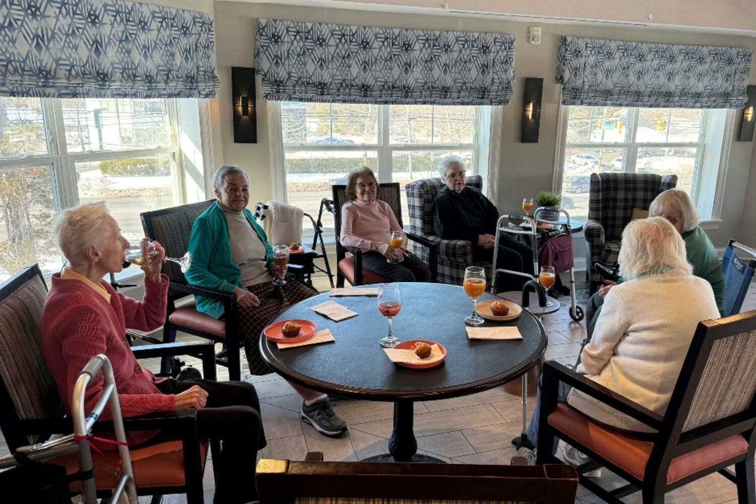 Residents socialize around tables in a bright common area at Arbor Terrace Monmouth, reflecting the warm community life of senior living in Shrewsbury, NJ.