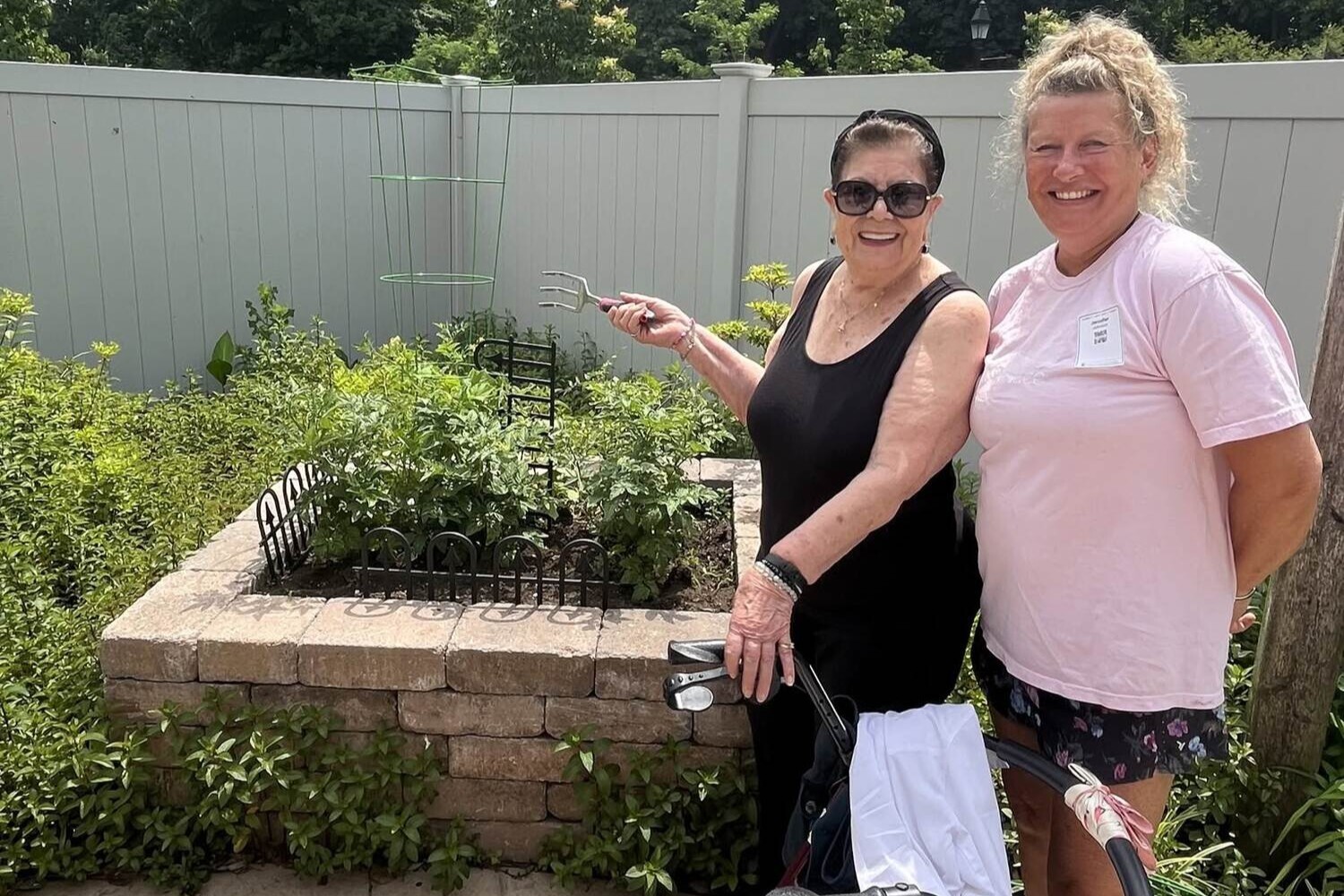Two people pose and smile beside a raised garden bed on the outdoor patio at Arbor Terrace Monmouth in Shrewsbury, NJ.