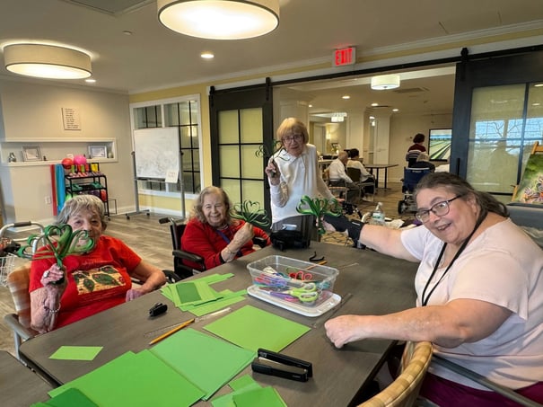 Residents and a staff member smile while crafting pipe cleaner shamrocks together at a table, reflecting the active senior lifestyle at this senior living community in Shrewsbury, NJ.