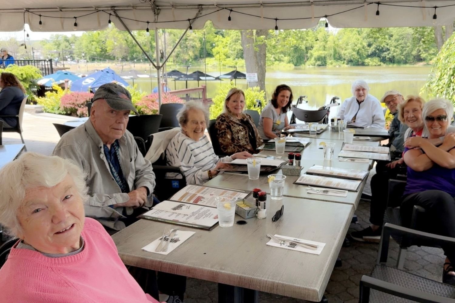 Residents and staff enjoy a scenic waterfront lunch outing together under a shaded tent, reflecting the active senior lifestyle at a senior living community in Morris Plains, NJ.