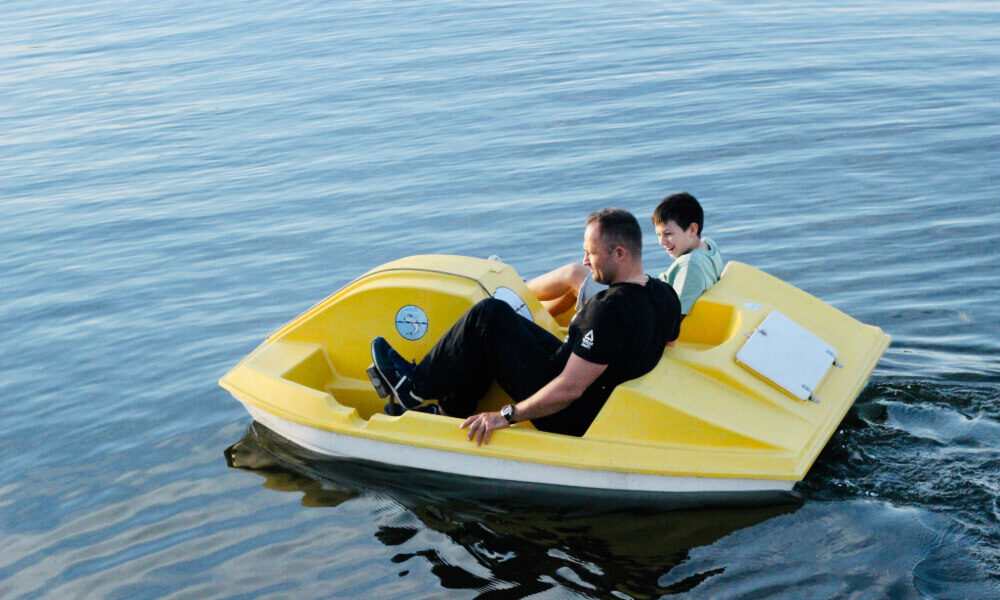 A father and child enjoying a fun moment on a yellow paddle boat in a serene lake.