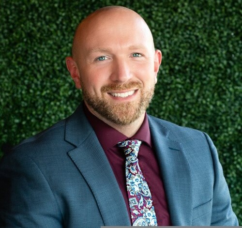 Professional headshot of Trevor, a team member at Arbor Terrace Morris Plains, with a well-groomed beard, wearing a suit and tie.