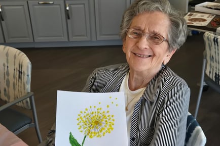 Resident holding up her drawing of a dandelion smiling 