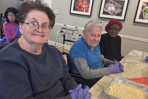 Residents sit together at a table wearing gloves while preparing food during a group activity