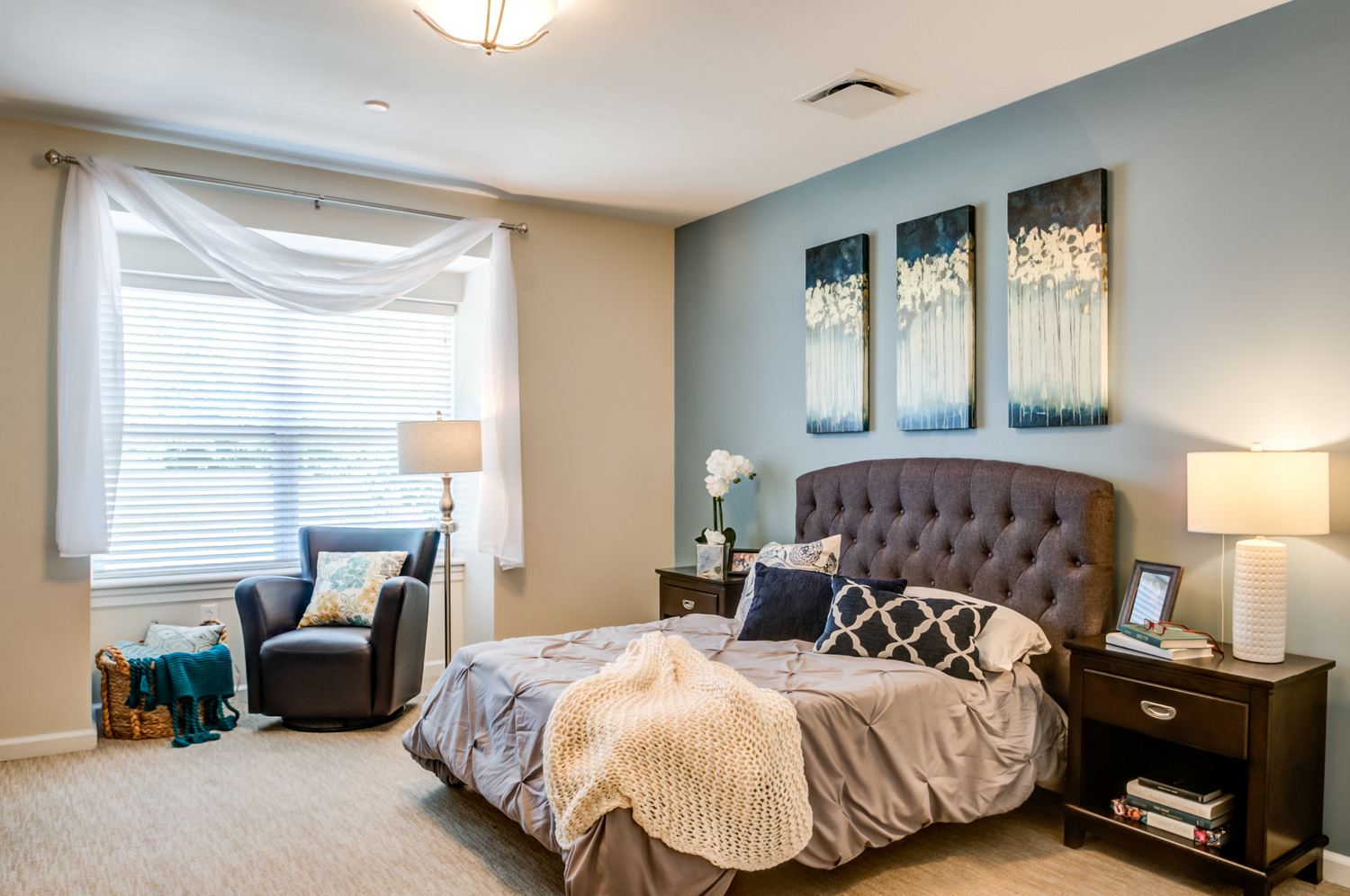 A cozy apartment bedroom at our senior living Mountainside NJ community features a tufted headboard, soft bedding, and a bright reading nook by the window, reflecting the comfortable, wellness-focused senior living Mountainside lifestyle.