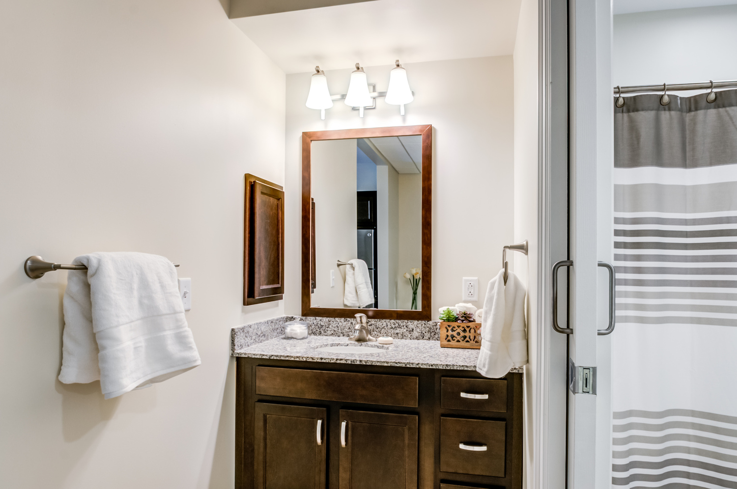 A well-appointed apartment bathroom at our senior living Mountainside NJ community features a granite vanity, framed mirror, and a walk-in shower, reflecting the comfortable, wellness-focused senior living Mountainside lifestyle.