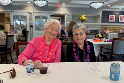 Two residents smile together wearing colorful leis during a festive gathering at our senior living Mountainside NJ community, capturing the joyful, active senior lifestyle North Jersey residents enjoy.