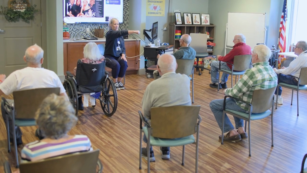 Residents enjoying a group activity session in the bright, welcoming common area at our assisted living community in Naperville, IL, with a staff member leading an engaging presentation for active senior living.
