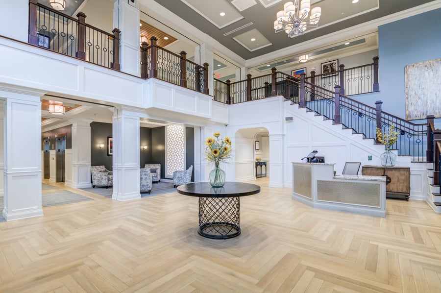 a high ceiling foyer with white walls, wooden floors, and an accent table underneath a chandelier