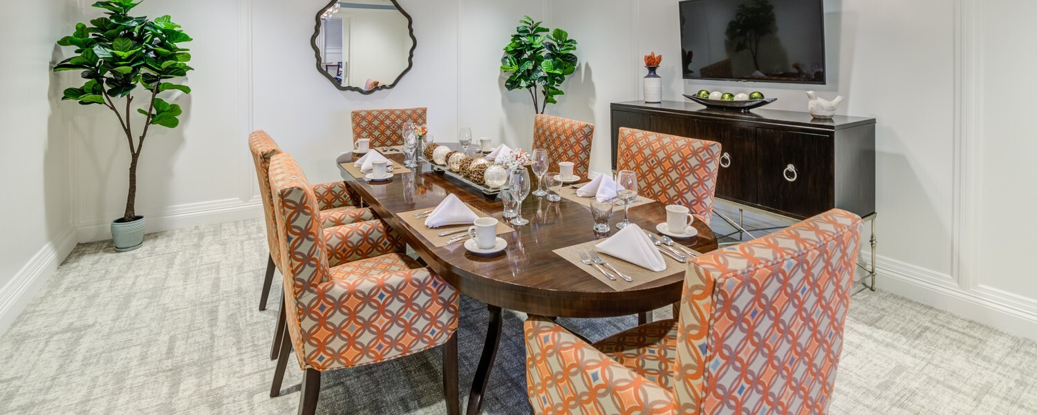 Elegant dining room with a wooden table set for six, patterned chairs, and greenery accents, reflecting the senior living Norwood NJ residents enjoy at this independent living Norwood NJ community.