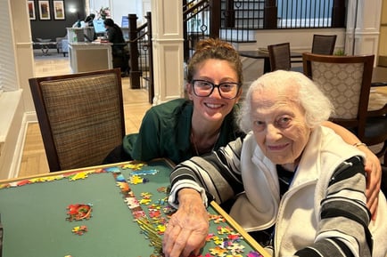 A staff member and an older resident smile warmly while working on a colorful puzzle together at Arbor Terrace Norwood, reflecting the personalized assisted living Norwood NJ families trust.