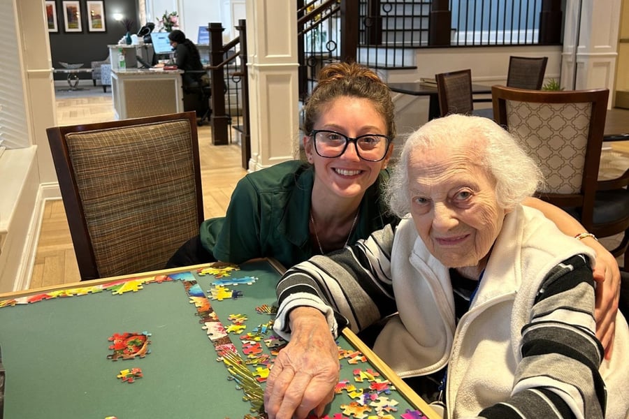 A staff member and an older resident smile warmly while working on a colorful puzzle together at Arbor Terrace Norwood, reflecting the personalized assisted living Norwood NJ families trust.