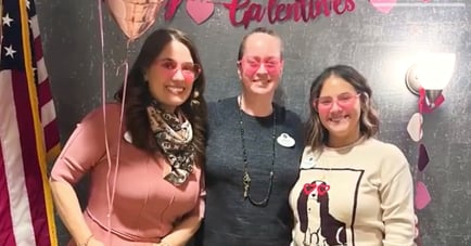 Three women smiling and posing together indoors, wearing casual clothing and accessories.