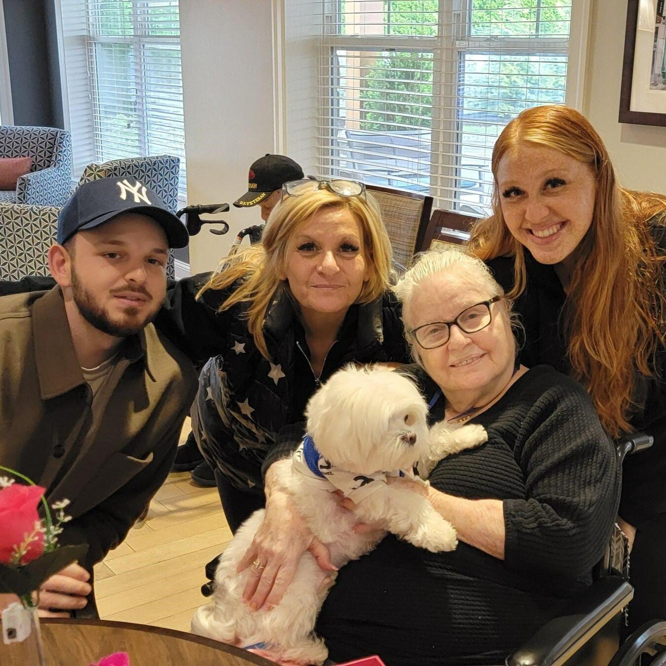 a resident hugging a dog with smiling with her loved ones during a celebration at a senior living community in Norwood, NJ
