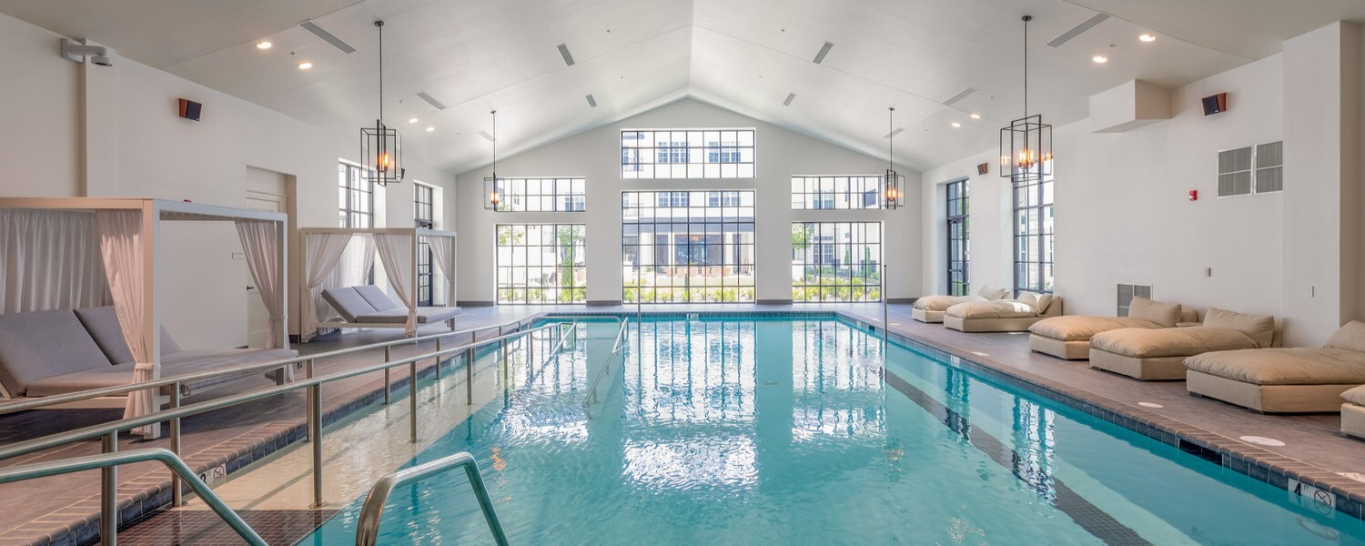 A bright, spacious indoor swimming pool at Opus East Memphis with vaulted ceilings, lounge seating, and canopy beds, reflecting the resort-style retirement living Memphis families value.