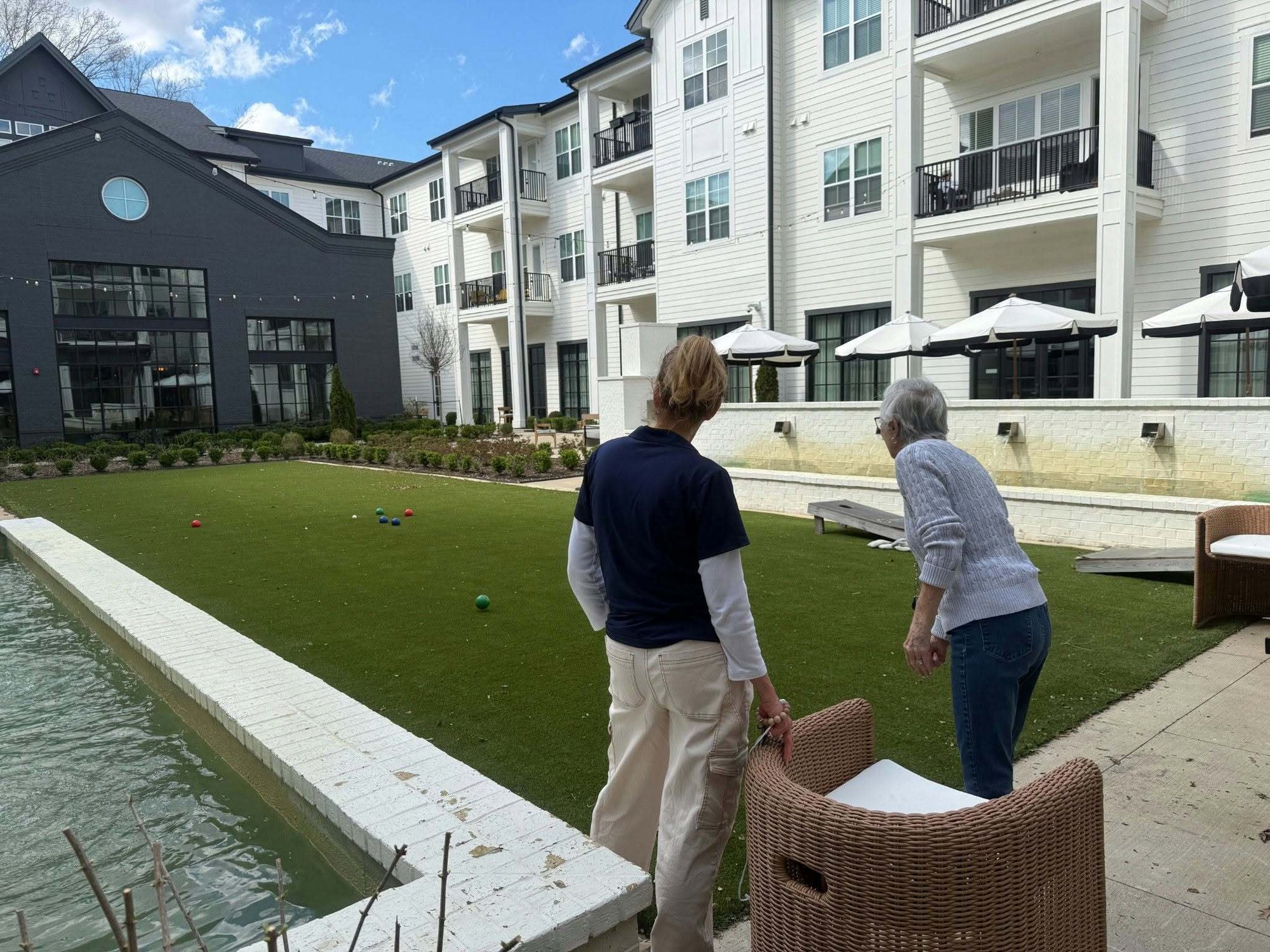 Two people stand overlooking a well-manicured bocce ball court in a beautifully landscaped outdoor courtyard, enjoying the active lifestyle at this retirement community in Memphis, Tennessee.