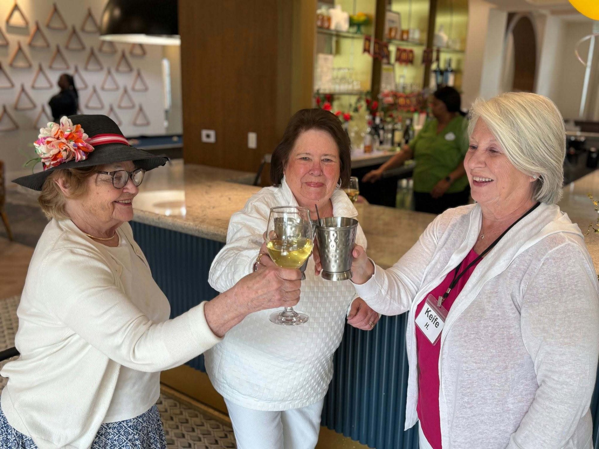 Three women share a cheerful toast together near a stylish bar area, celebrating friendship and connection as part of an active senior lifestyle at The Arbor Company.
