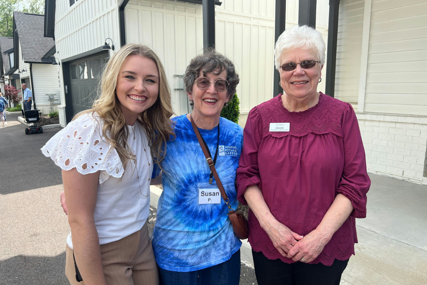 2 female residents with Opus East Memphis team member in front of cottages