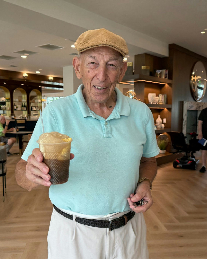 A man smiles and holds an iced coffee drink in the stylish common area at Opus East Memphis, showcasing the everyday enjoyment and vibrant senior living experience in East Memphis, TN.